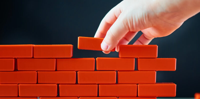 Hand puts last brick on wall. Concept of construction and building